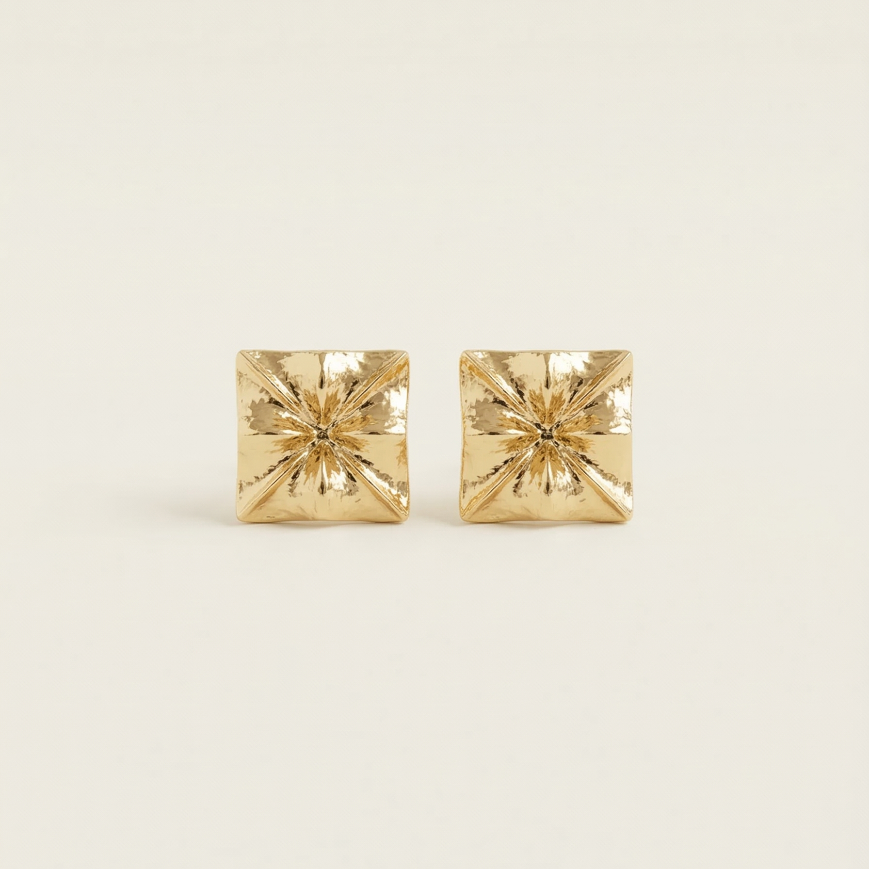 Pair of gold square stud earrings on a light beige background