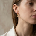 Close-up of a woman wearing gold triangular earrings against a neutral background