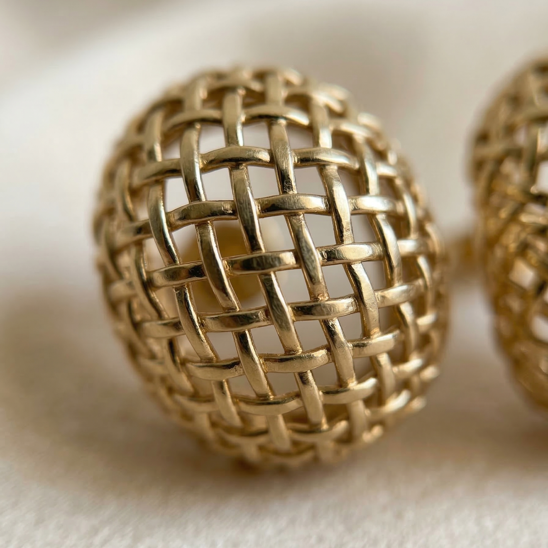 Gold woven sphere earrings on a beige fabric background