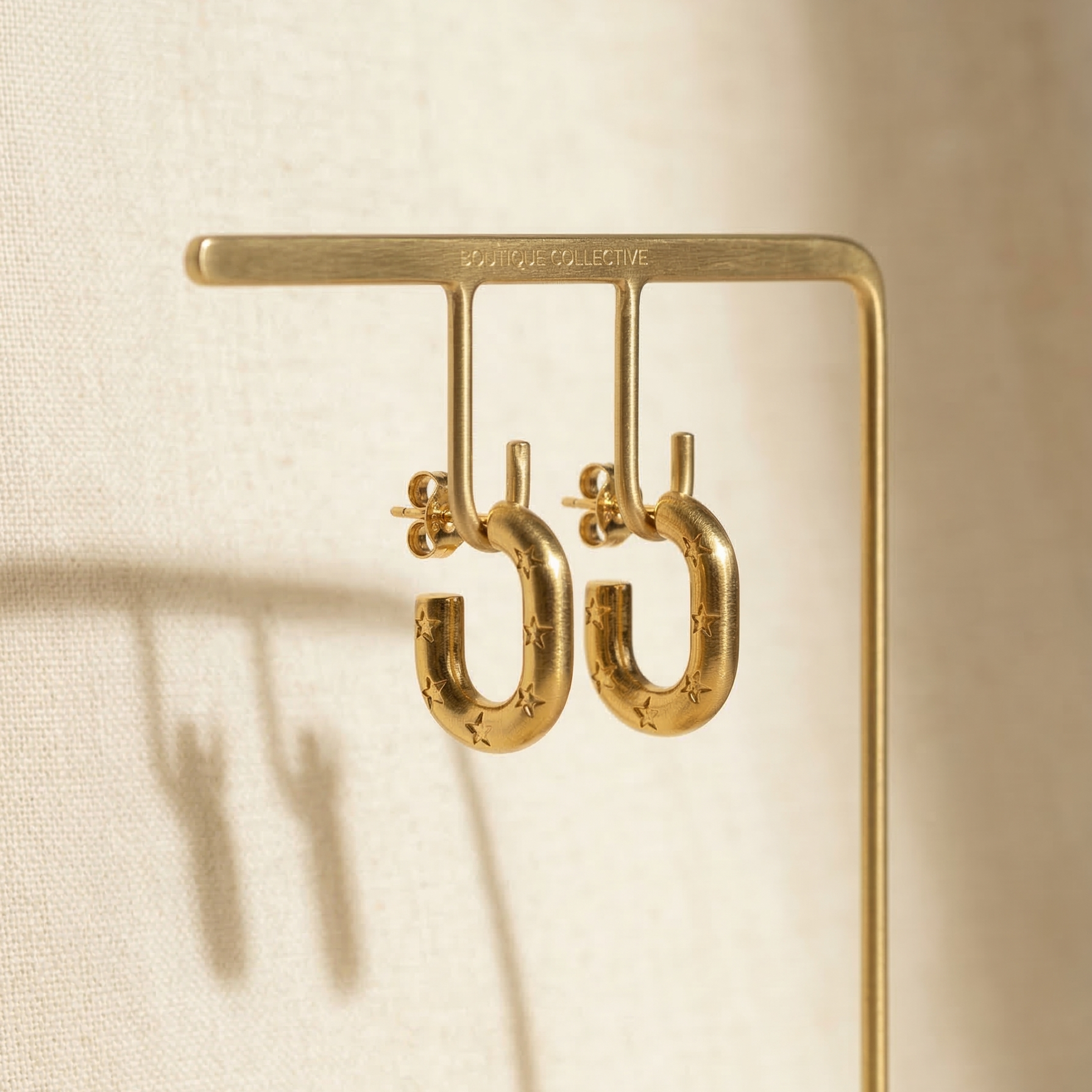 Gold earrings on a stand against a beige background