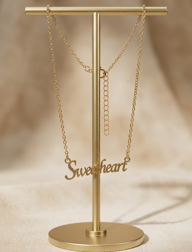 Gold 'Sweetheart' necklace on a gold stand against a beige background