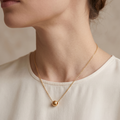 Close-up of a person wearing a gold necklace with a small pendant on a neutral background