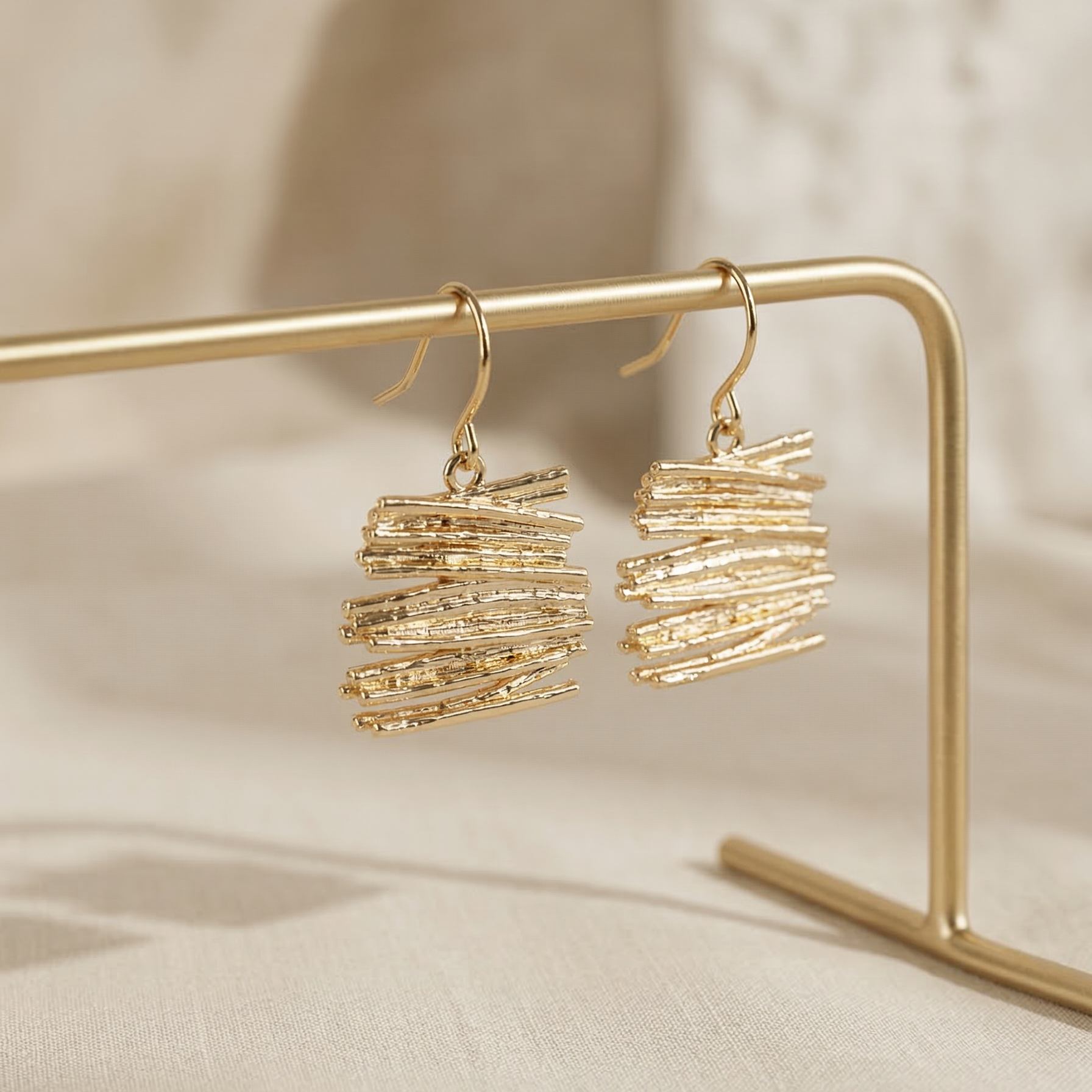 Gold earrings on a gold stand against a beige background