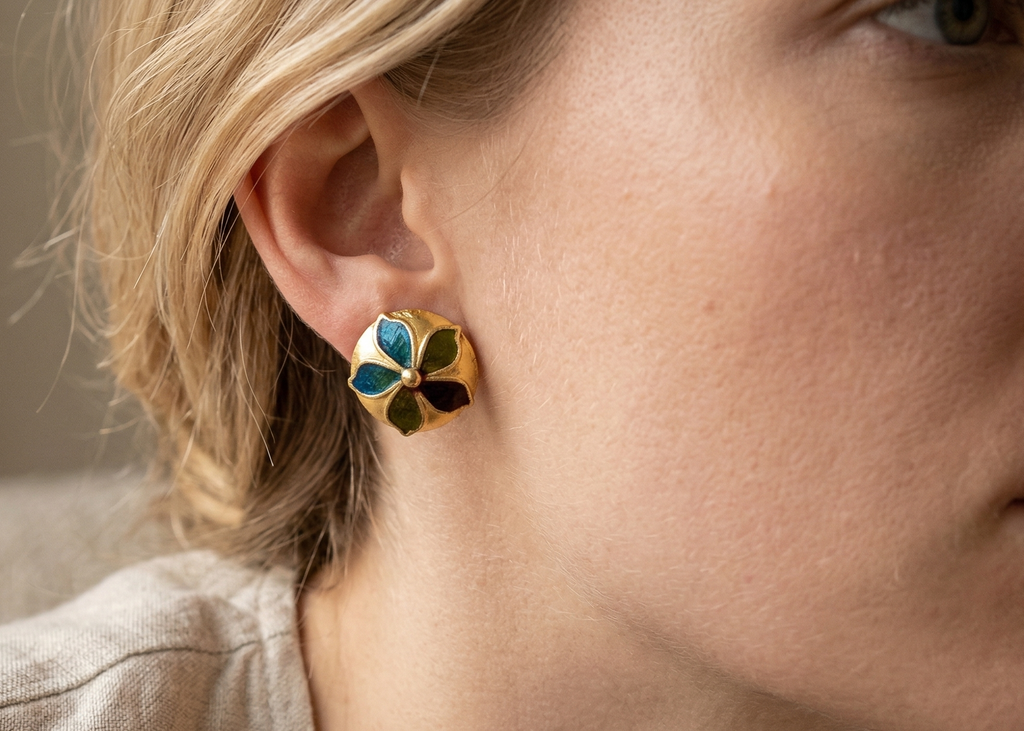 Close-up of a person wearing a floral earring with gold and green details.
