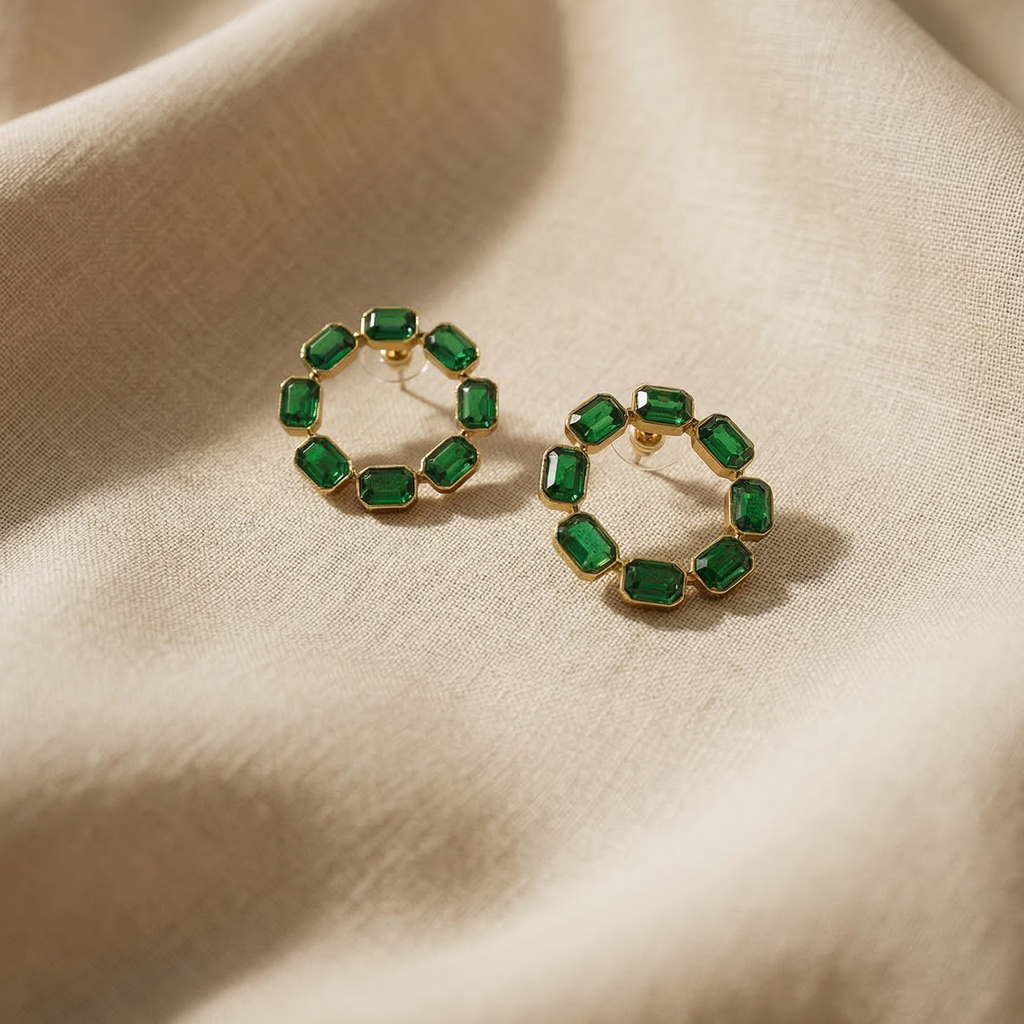 Gold hoop earrings with green gemstones on a beige fabric background
