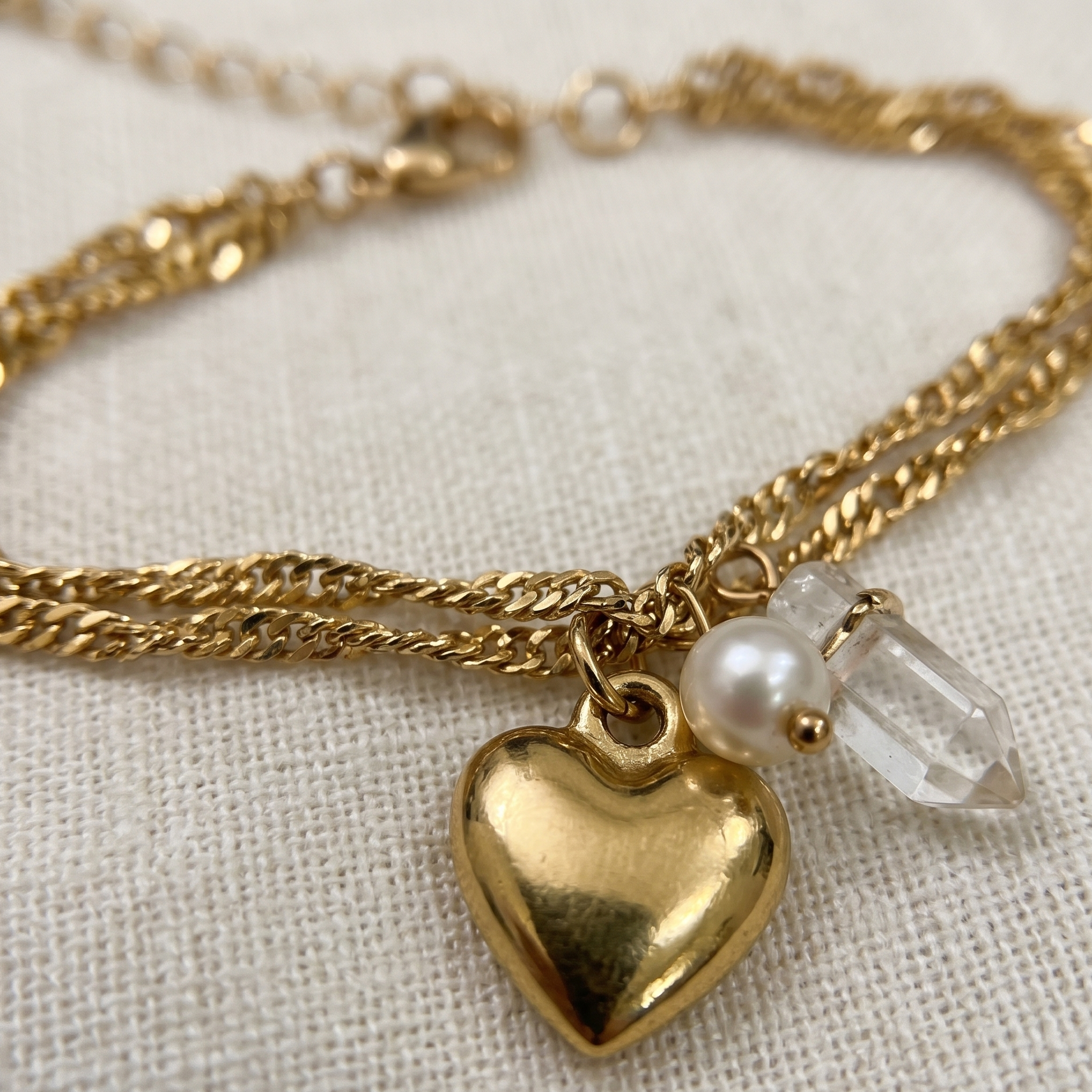 Gold heart-shaped pendant necklace with pearl and crystal charm on a light fabric background
