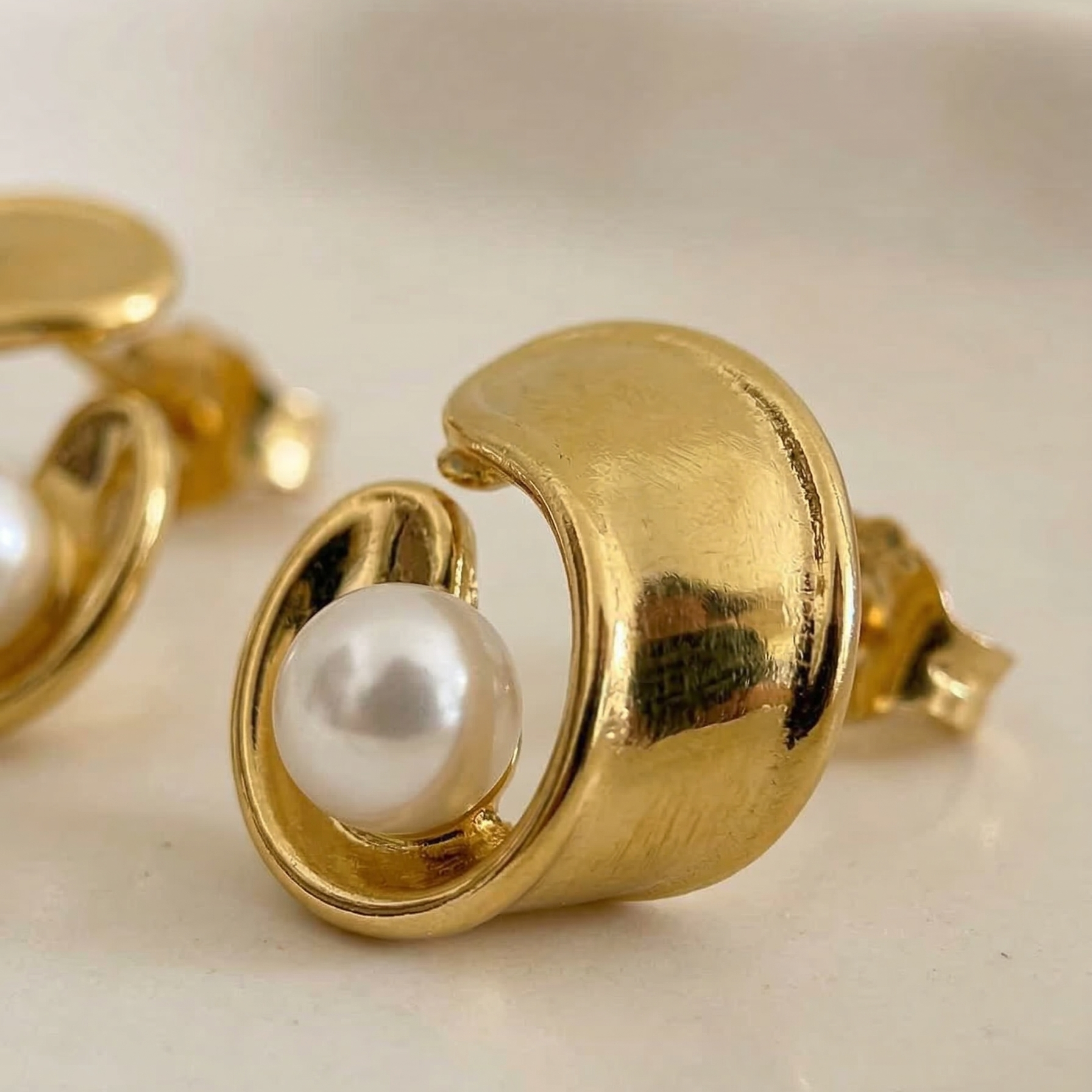 Gold earrings with pearl center on a light background