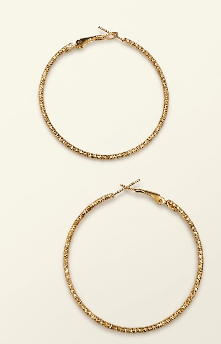 Two gold hoop earrings on a light beige background