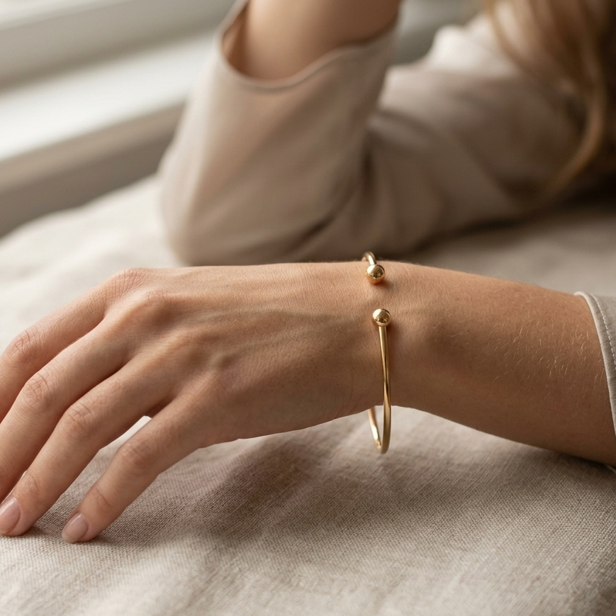 Close-up of a hand wearing a gold bracelet on a neutral background