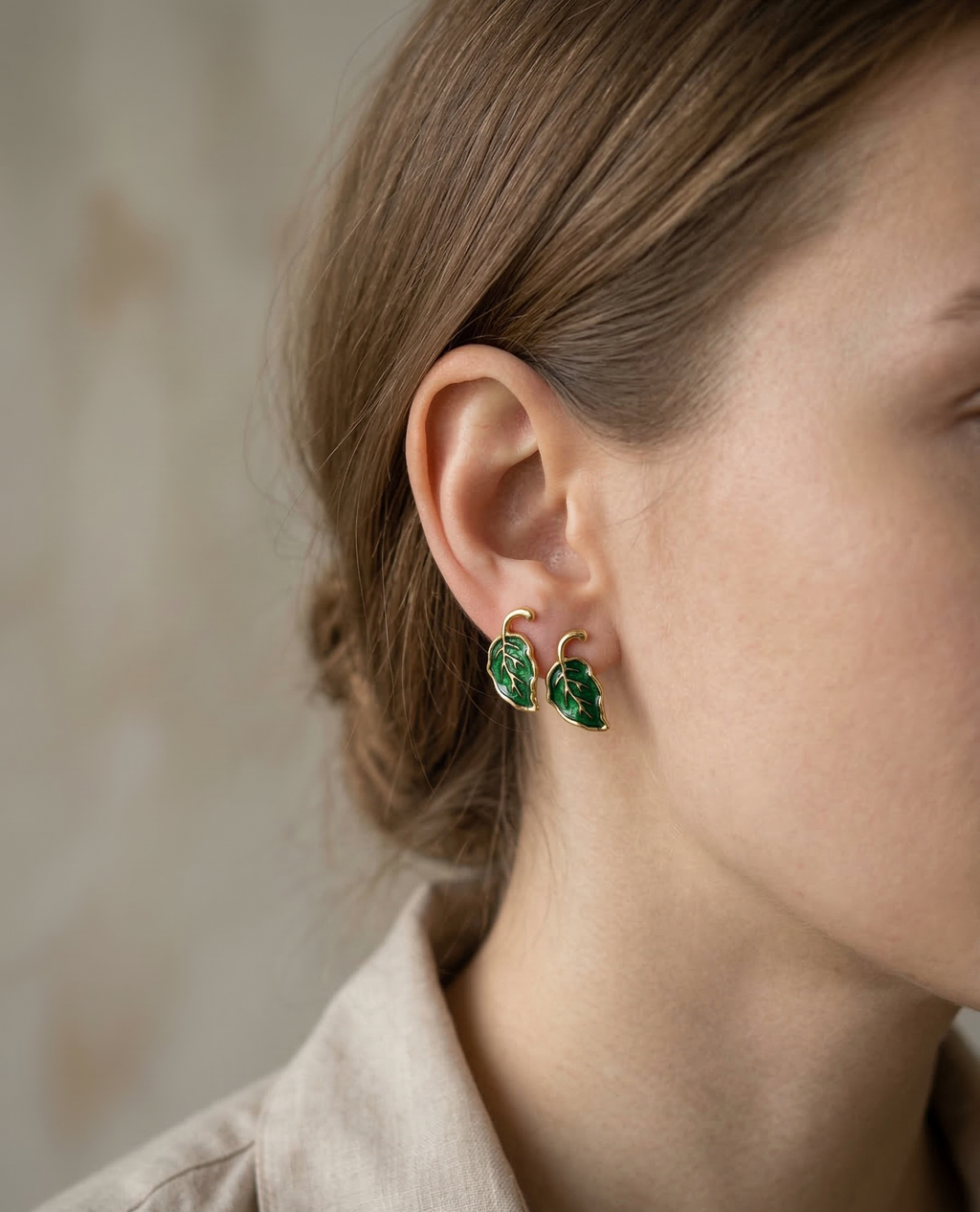 Close-up of a person wearing green leaf-shaped earrings with a neutral background