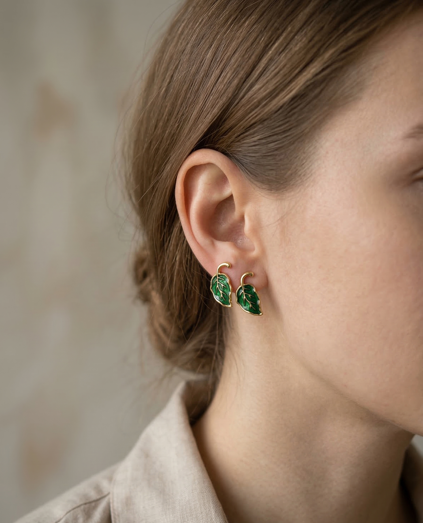 Close-up of a person wearing green leaf-shaped earrings with a neutral background
