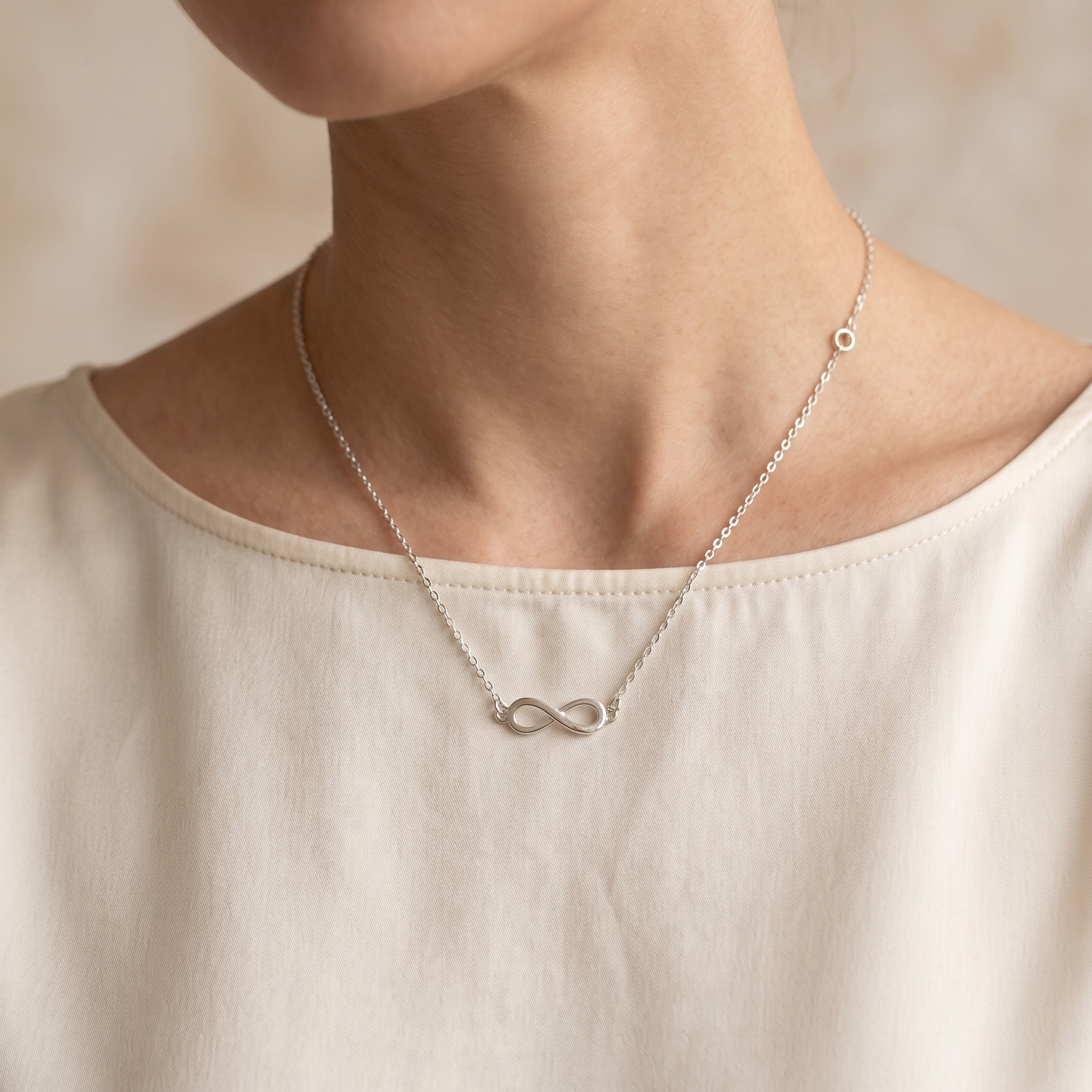 Woman wearing a silver infinity necklace against a neutral background