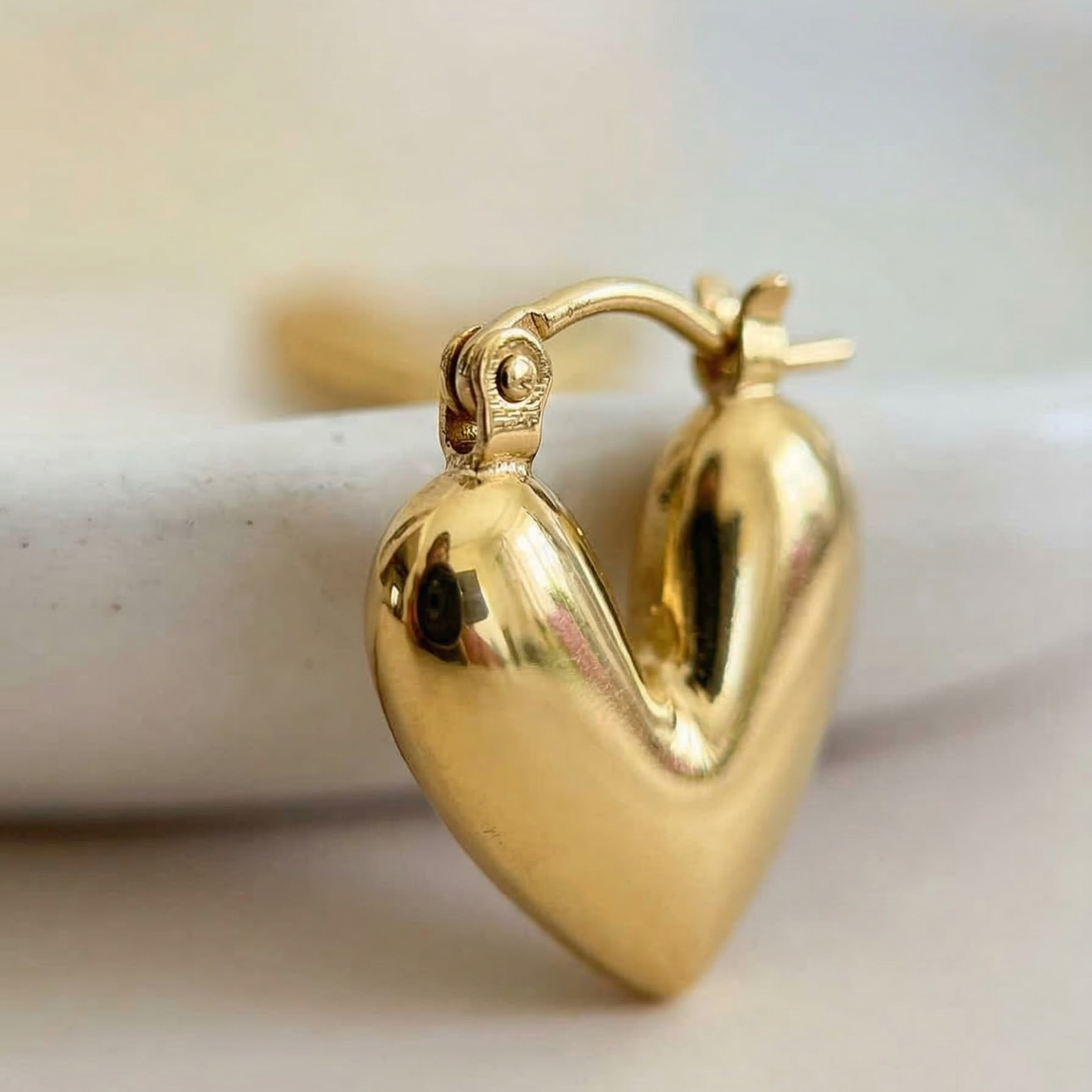 Gold heart-shaped hoop earring on a light background