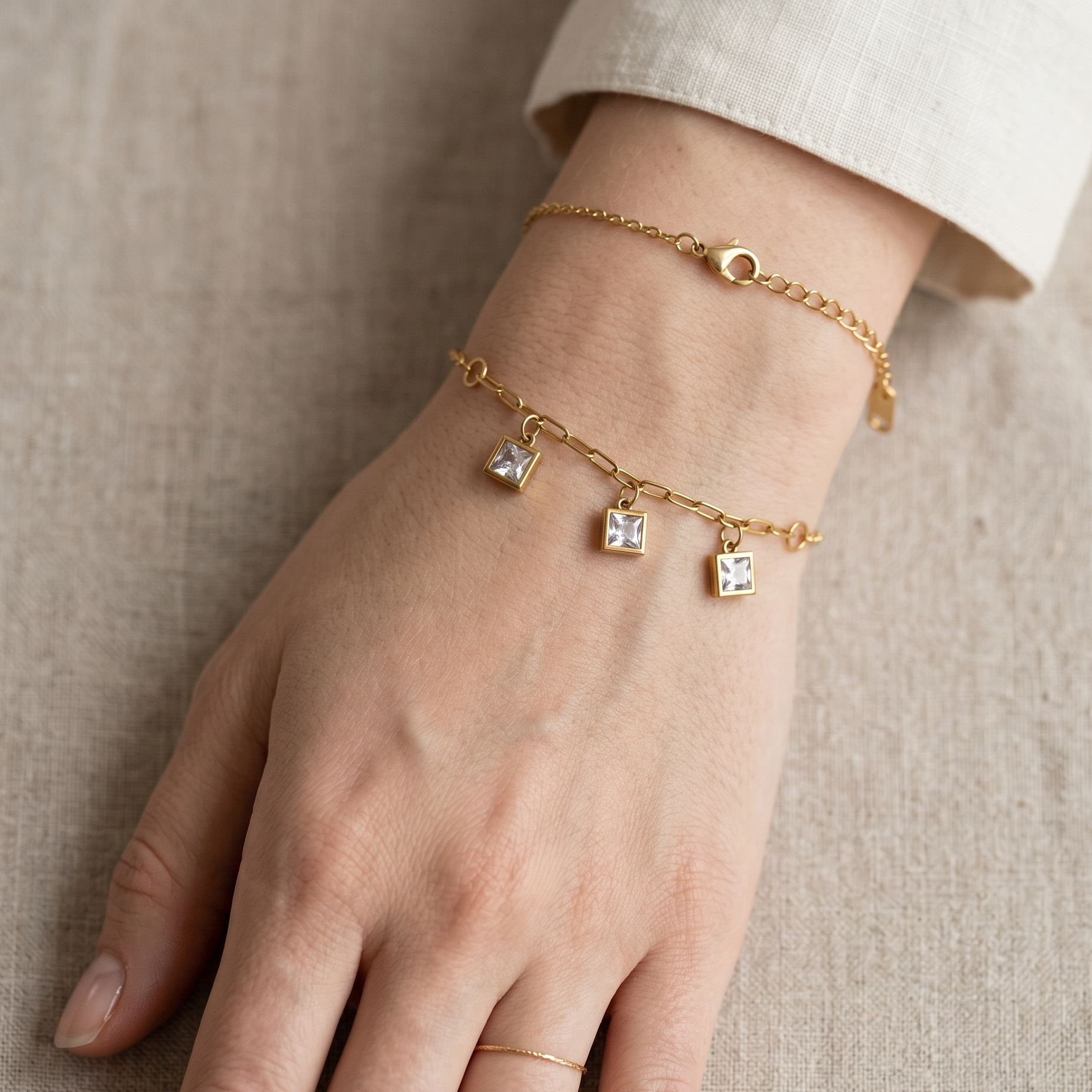 Gold bracelet with charms on a wrist against a neutral background