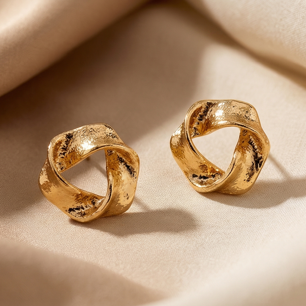 Pair of gold earrings on a beige fabric background