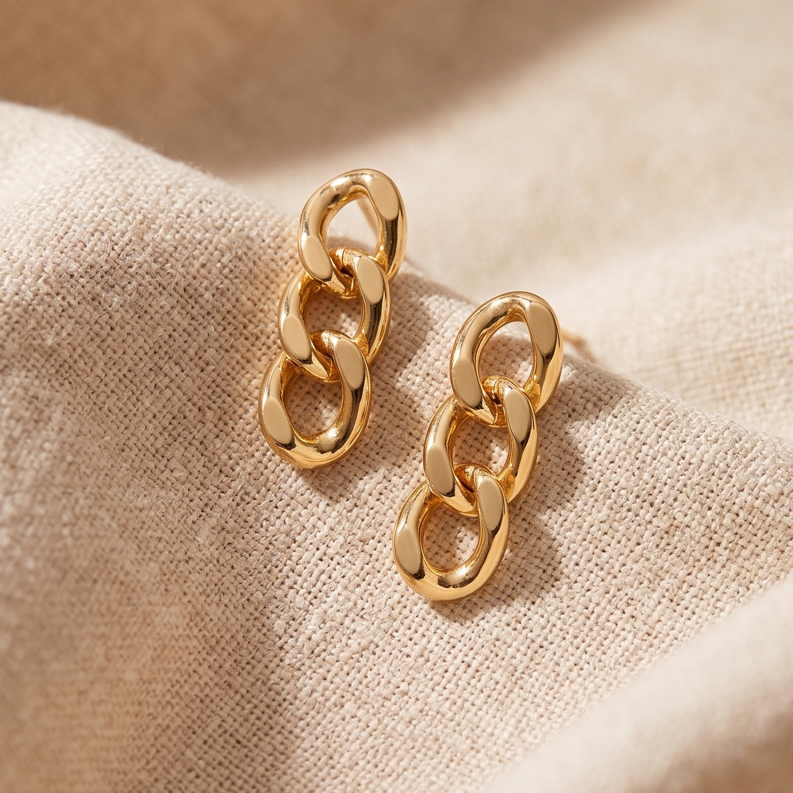 Gold chain earrings on a beige fabric background