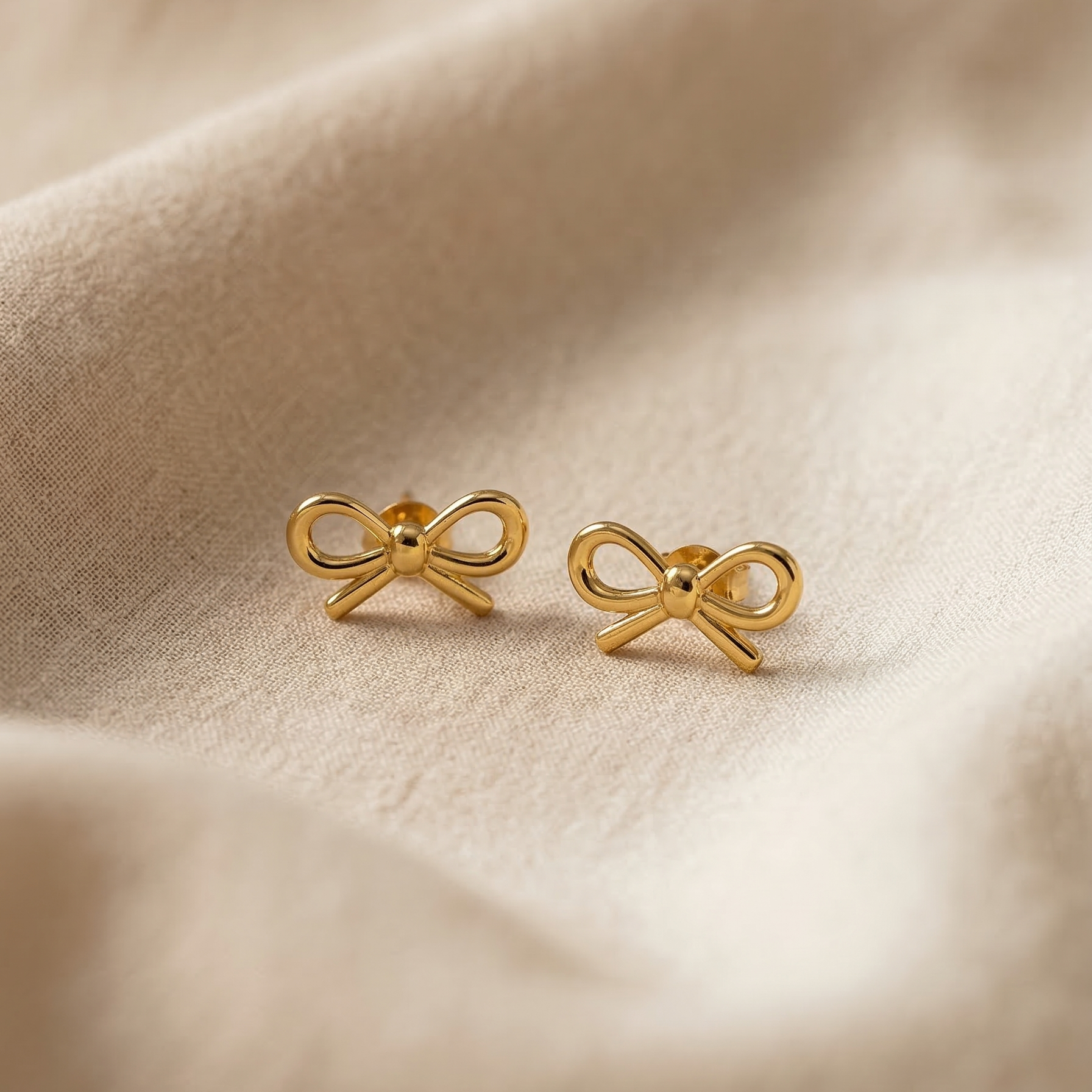 Gold bow-shaped earrings on a beige fabric background