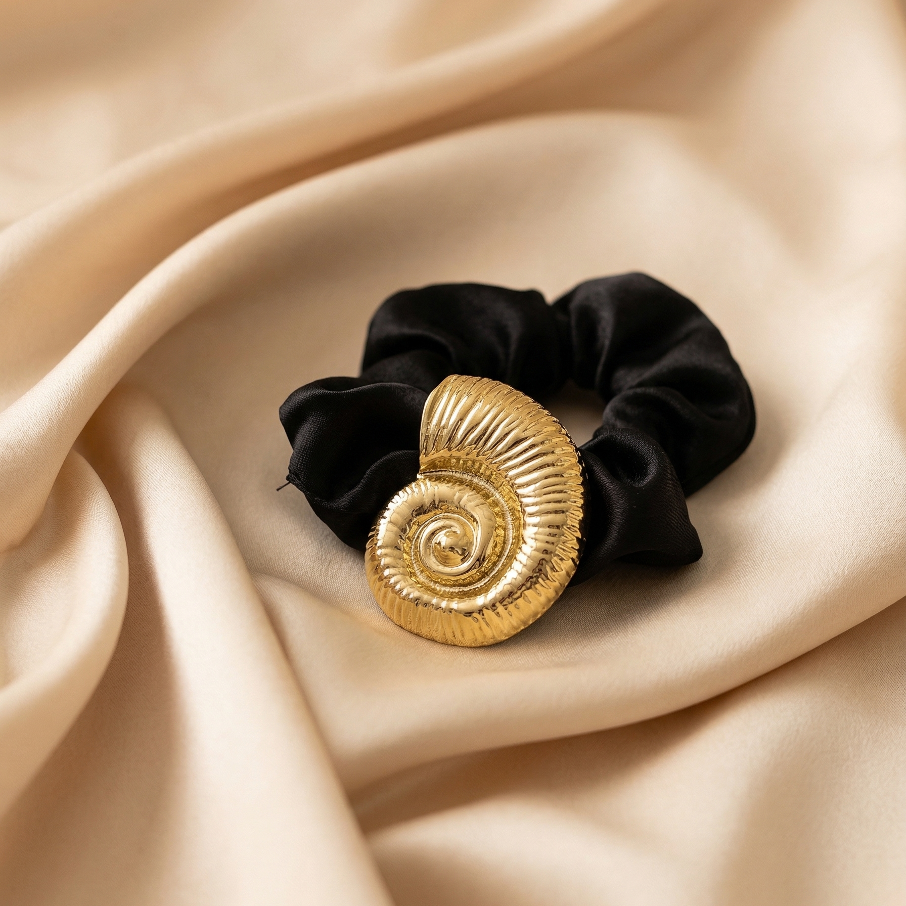Black scrunchie with gold spiral design on a beige fabric background