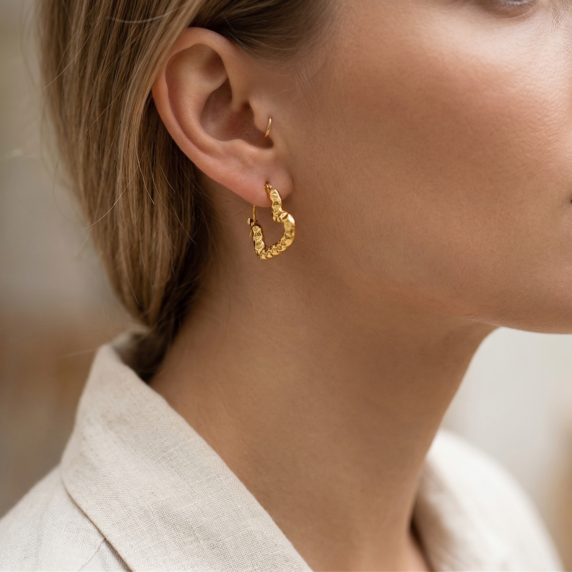 Close-up of a person wearing gold hoop earrings with a blurred background