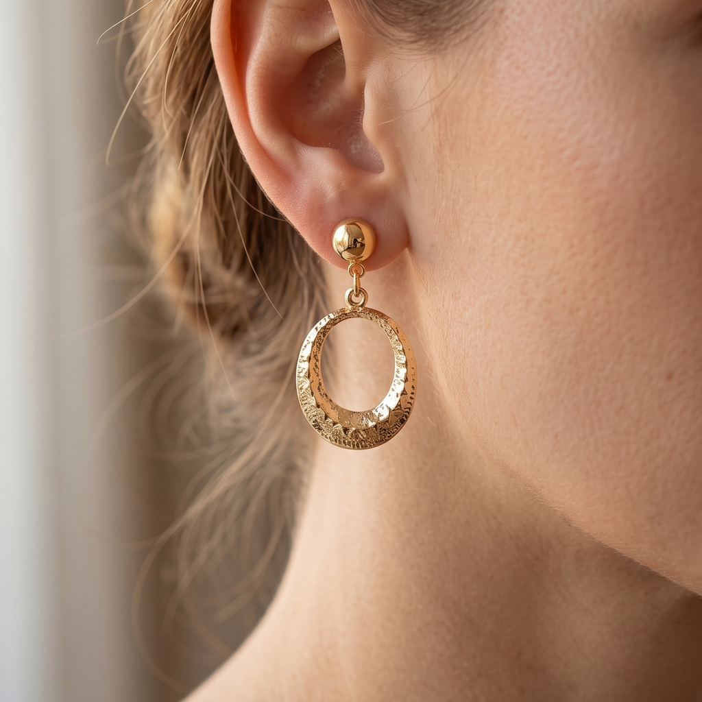 Close-up of a person wearing gold hoop earrings with a neutral background
