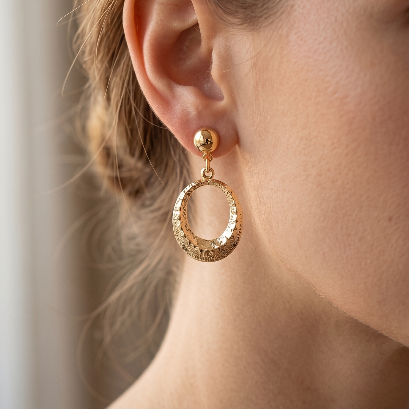 Close-up of a person wearing gold hoop earrings with a neutral background