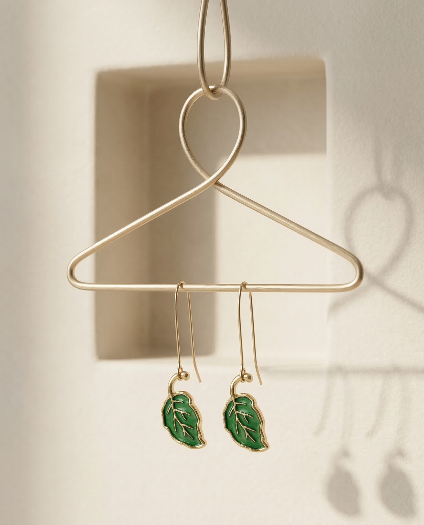 Green leaf-shaped earrings hanging on a gold hanger against a neutral background