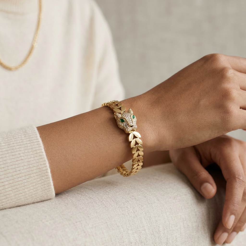 Gold bracelet with a green stone worn on a wrist against a neutral background