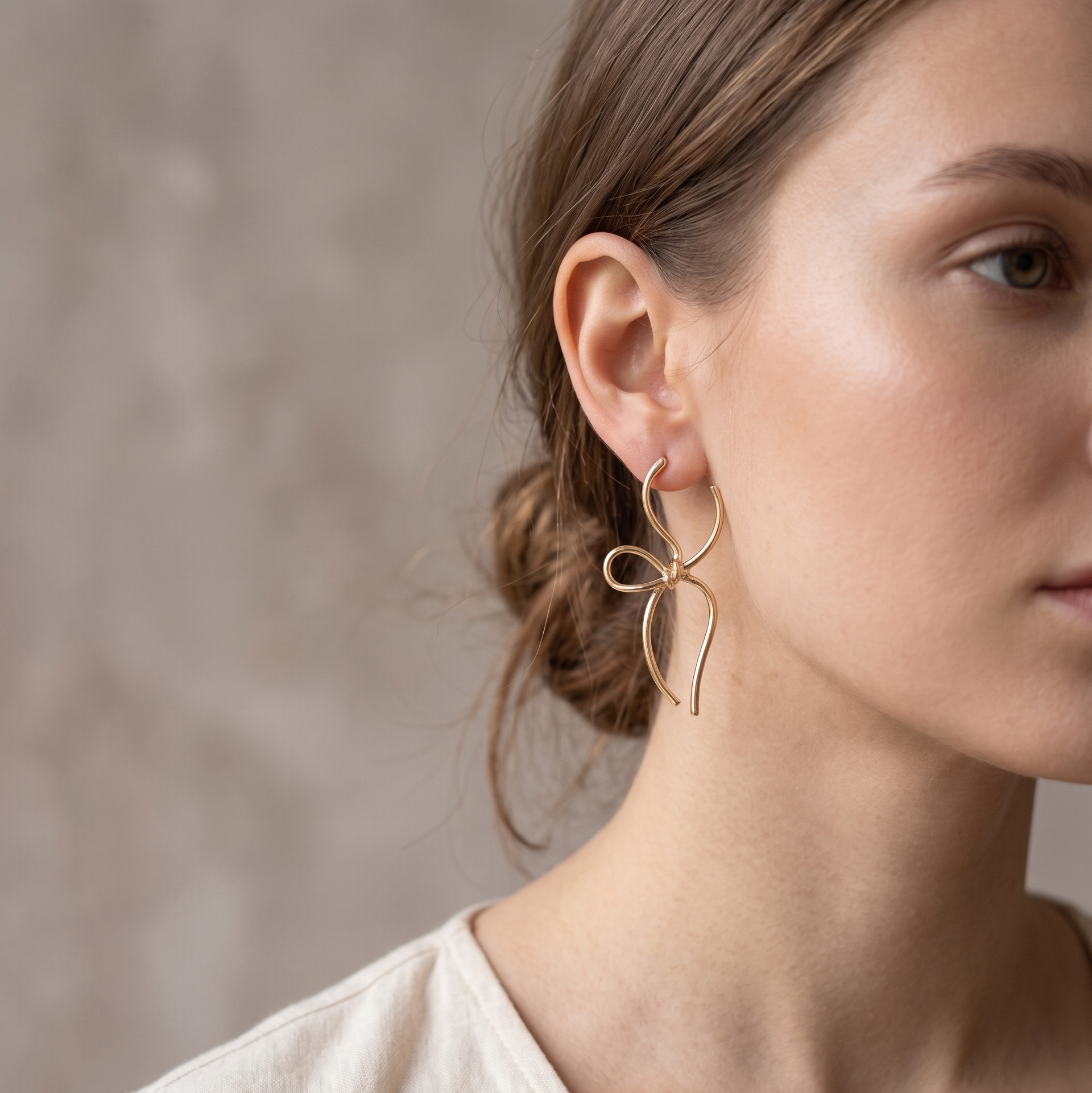 Close-up of a woman wearing a gold earring against a neutral background