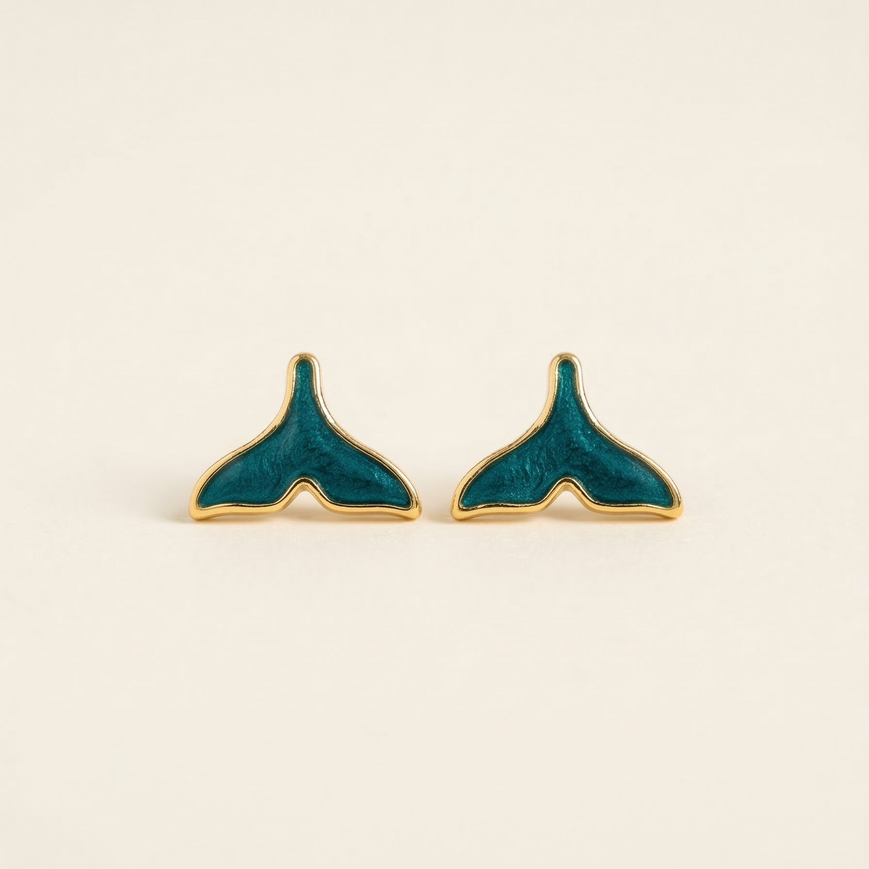 Teal and gold whale tail earrings on a beige background