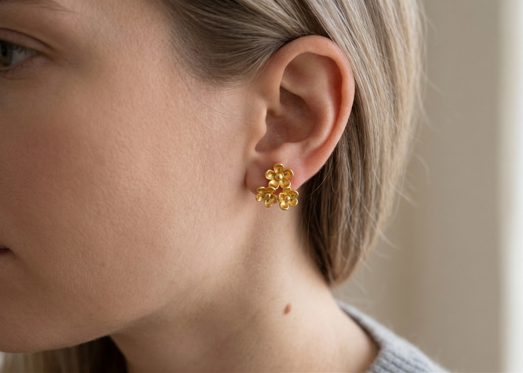 Close-up of a person wearing gold floral earrings with a neutral background