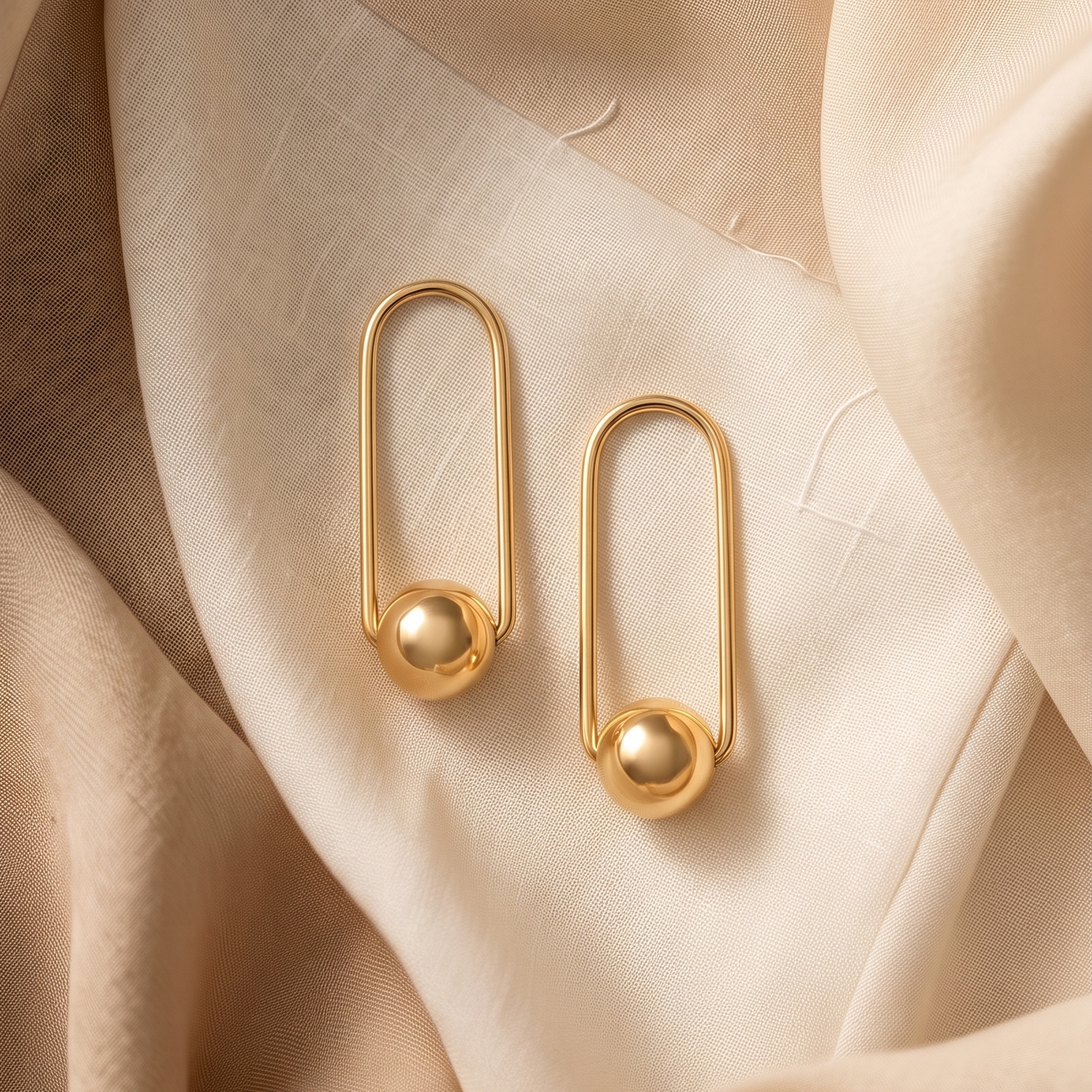 Gold safety pin earrings on a soft beige fabric background