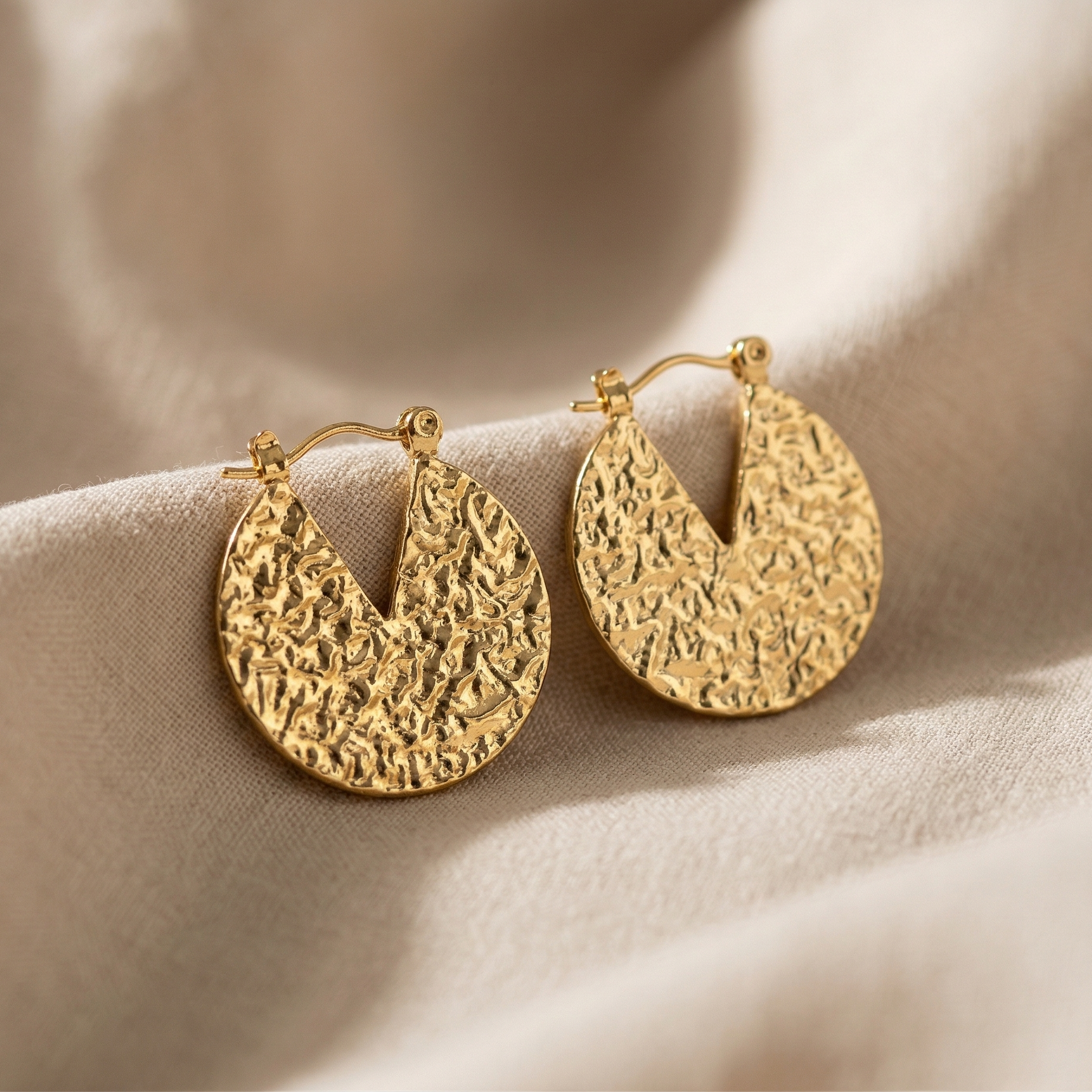 Gold hoop earrings on a soft beige fabric background