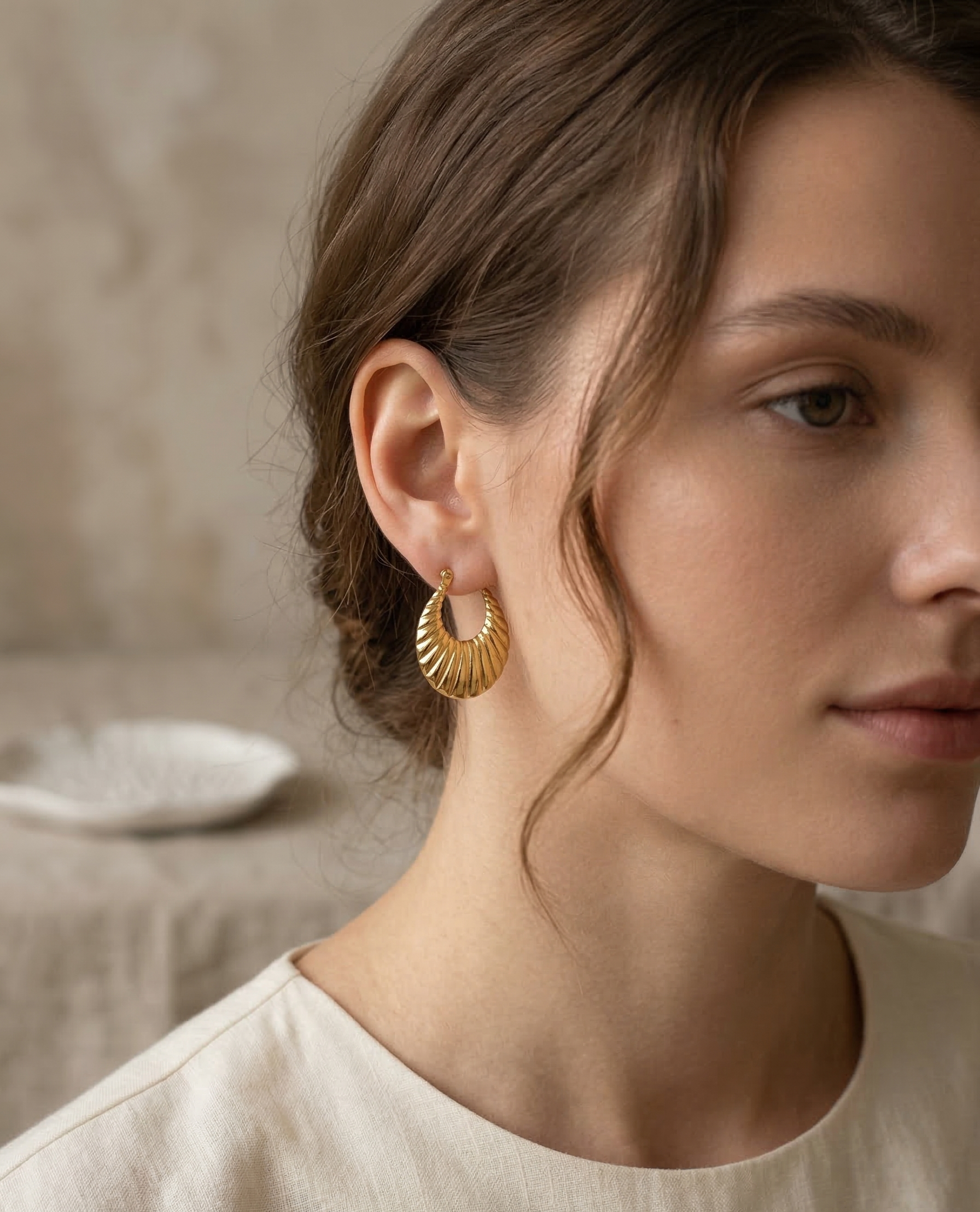 Close-up of a woman wearing gold hoop earrings with a neutral background