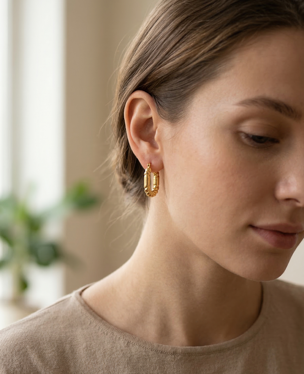 Woman wearing gold hoop earrings with a blurred indoor background