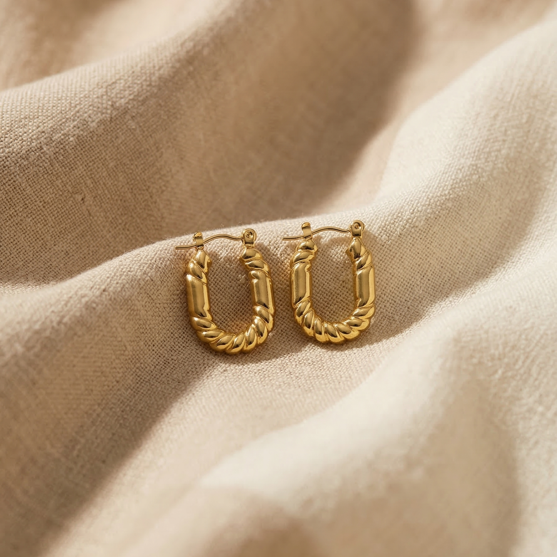 Gold hoop earrings on a beige fabric background