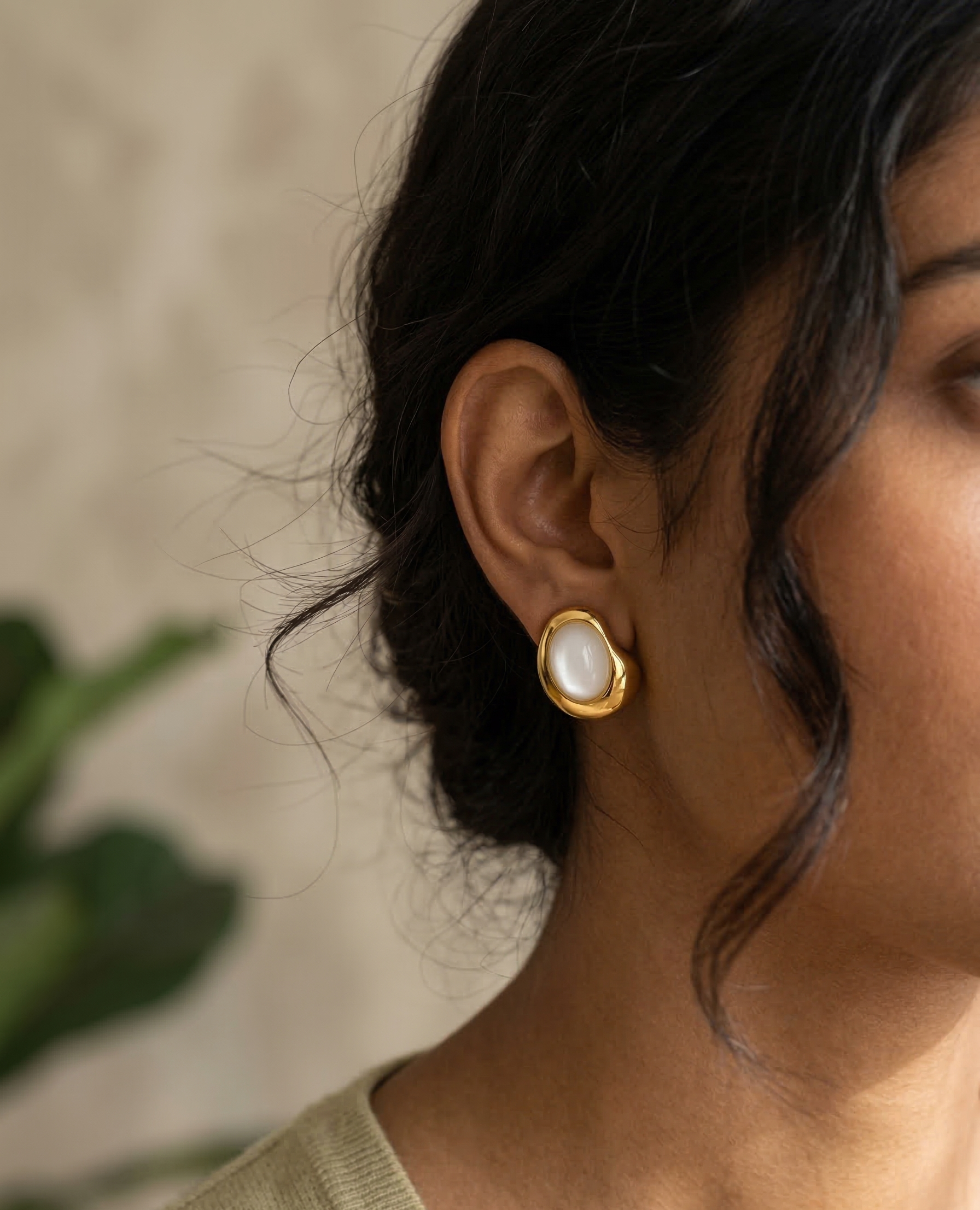 Close-up of a person wearing gold earrings with a blurred background
