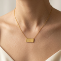 Gold necklace with a rectangular pendant on a person wearing a white garment.