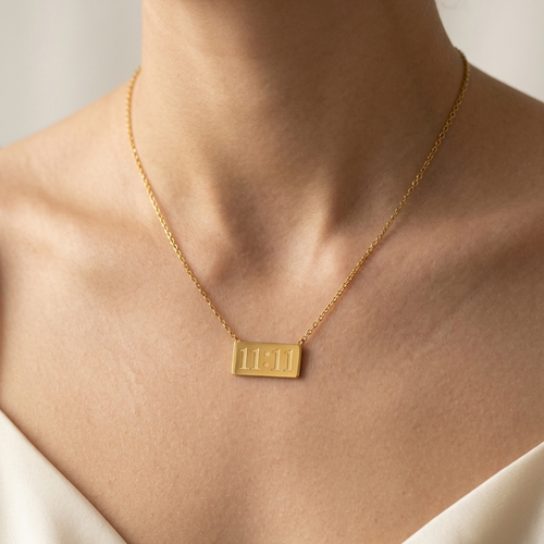 Gold necklace with a rectangular pendant on a person wearing a white garment.