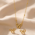 Gold bow-shaped necklace and earrings on a beige fabric background