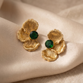 Gold earrings with green gemstones on a beige fabric background