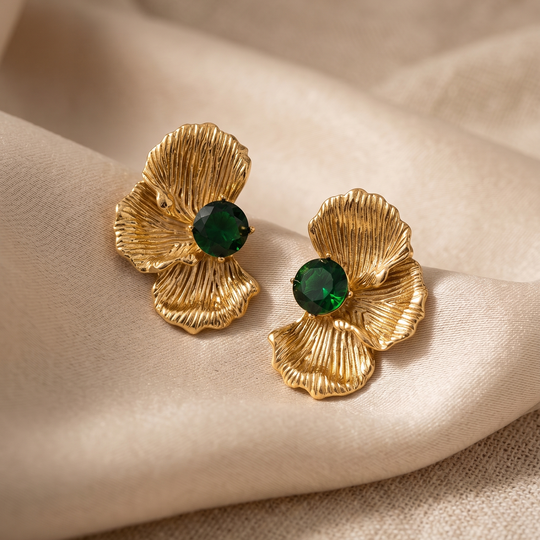 Gold earrings with green gemstones on a beige fabric background