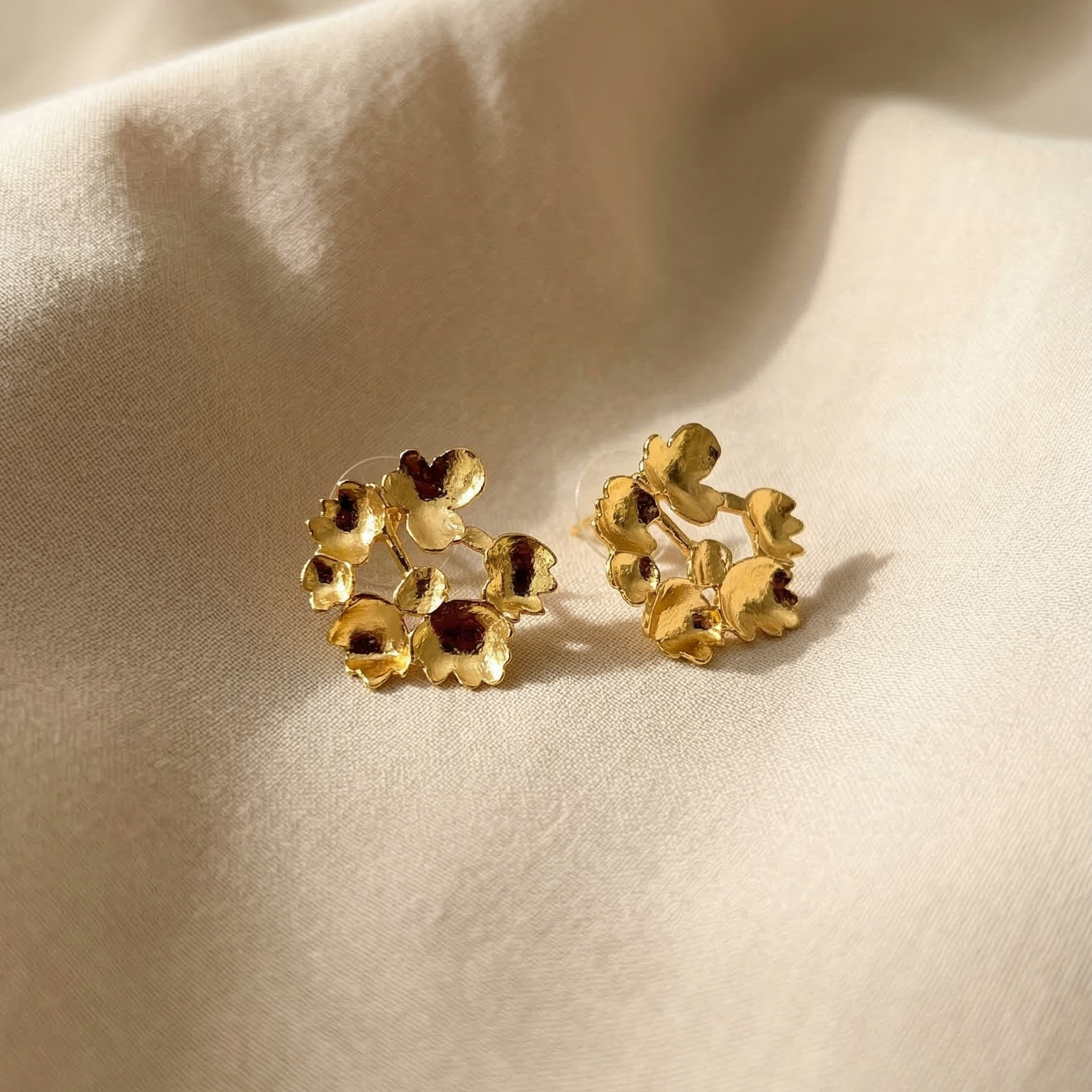 Gold floral earrings on a beige fabric background