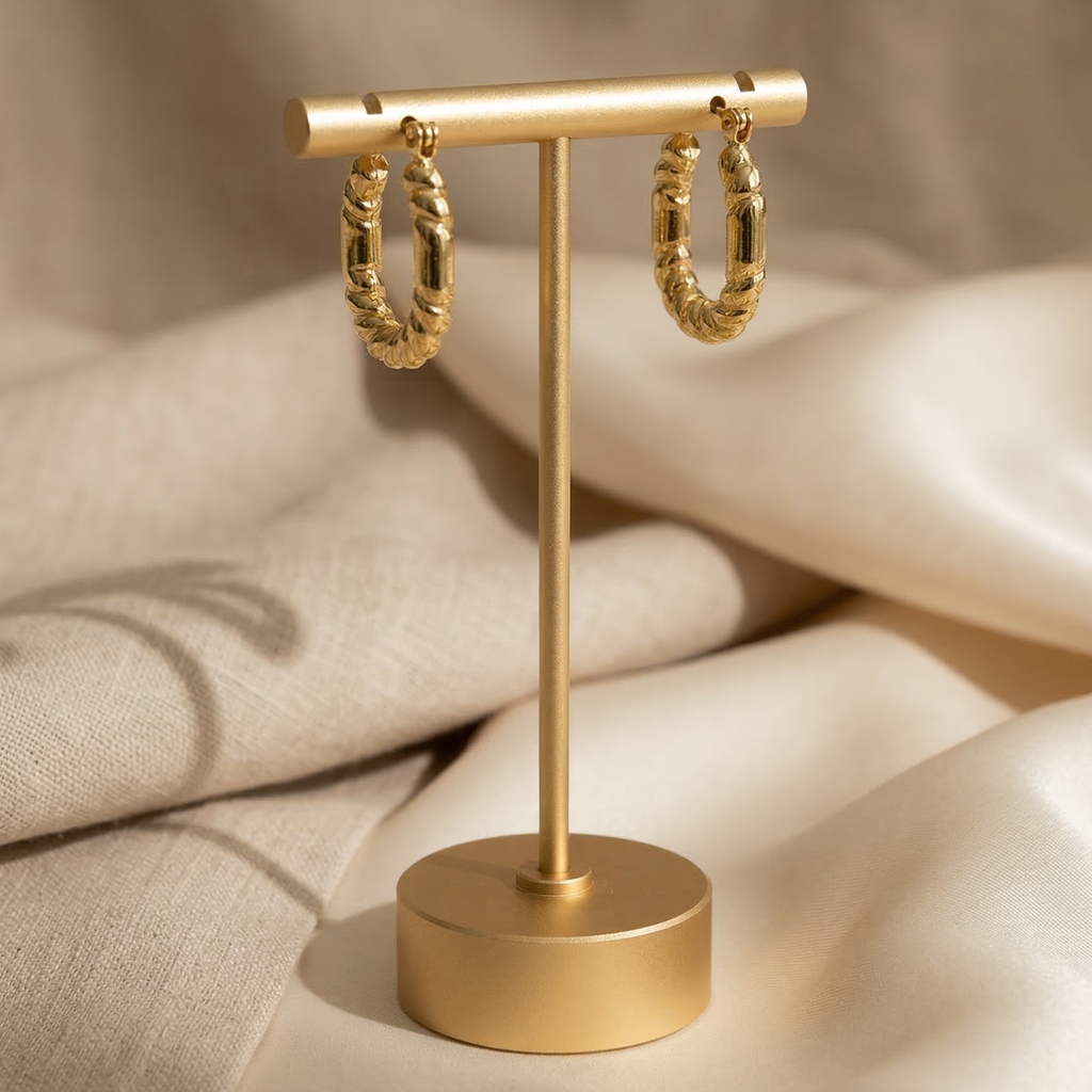 Gold hoop earrings on a matching gold stand against a beige fabric background