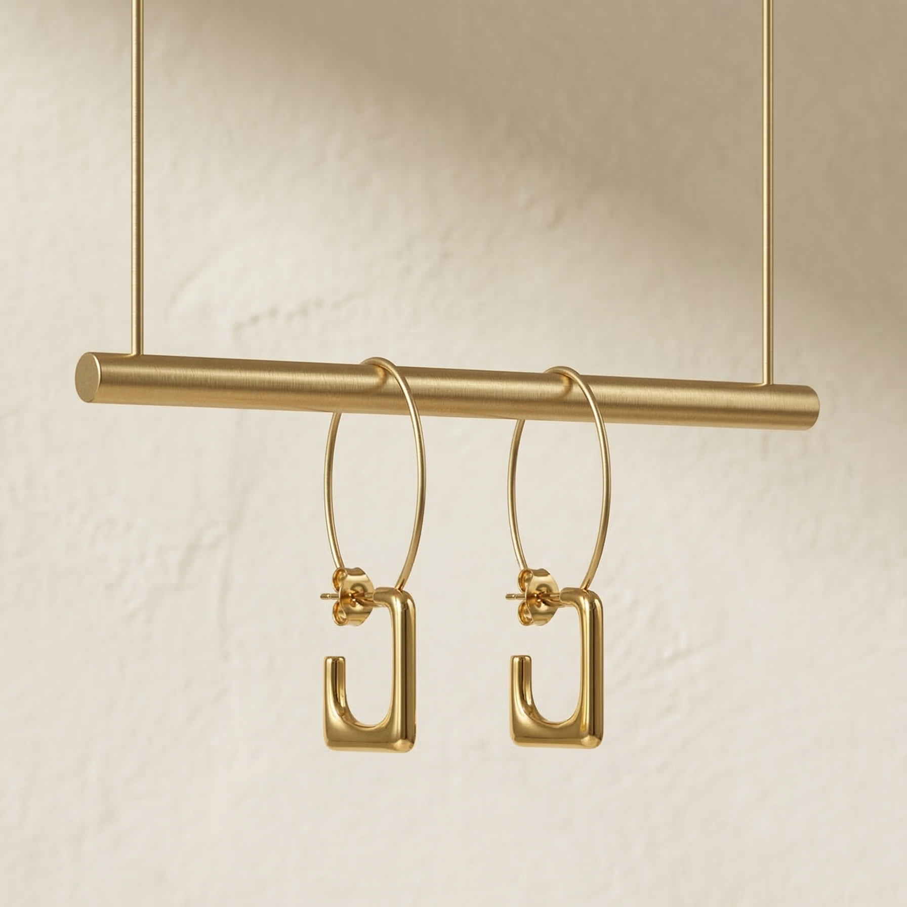Gold hoop earrings on a gold bar against a beige background