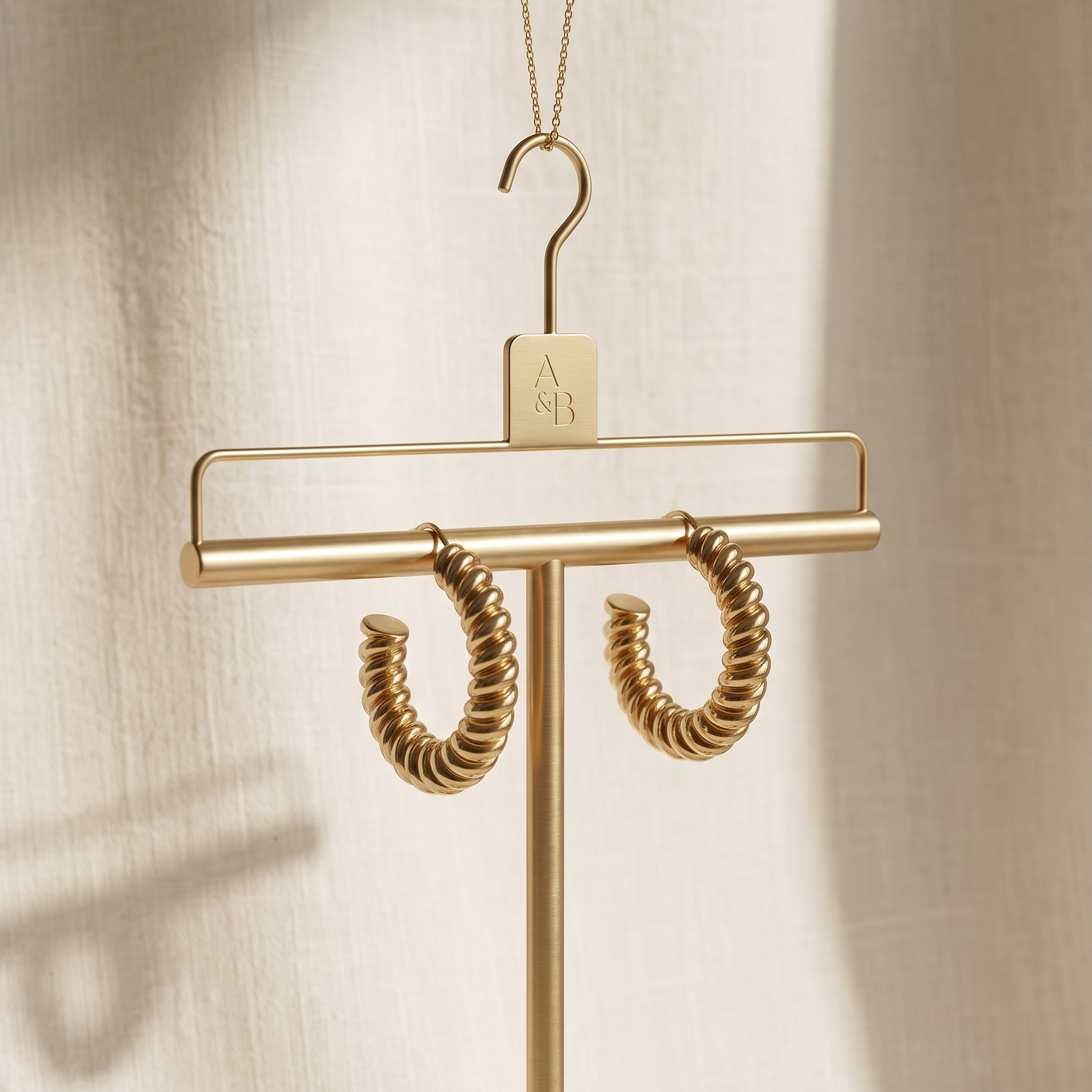 Gold hoop earrings hanging on a gold hanger against a beige background