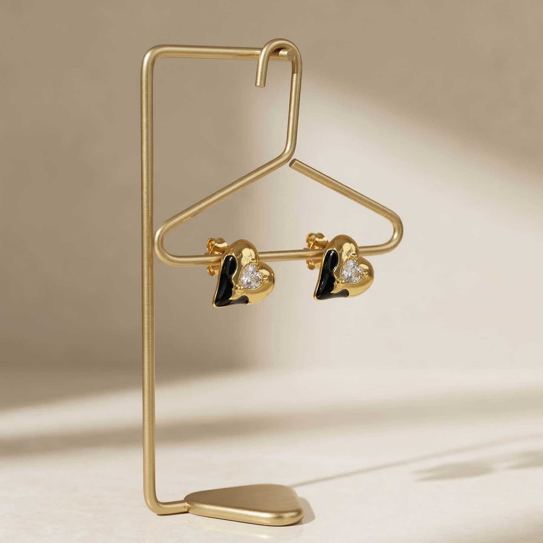 Gold earring stand with heart-shaped earrings on a beige background