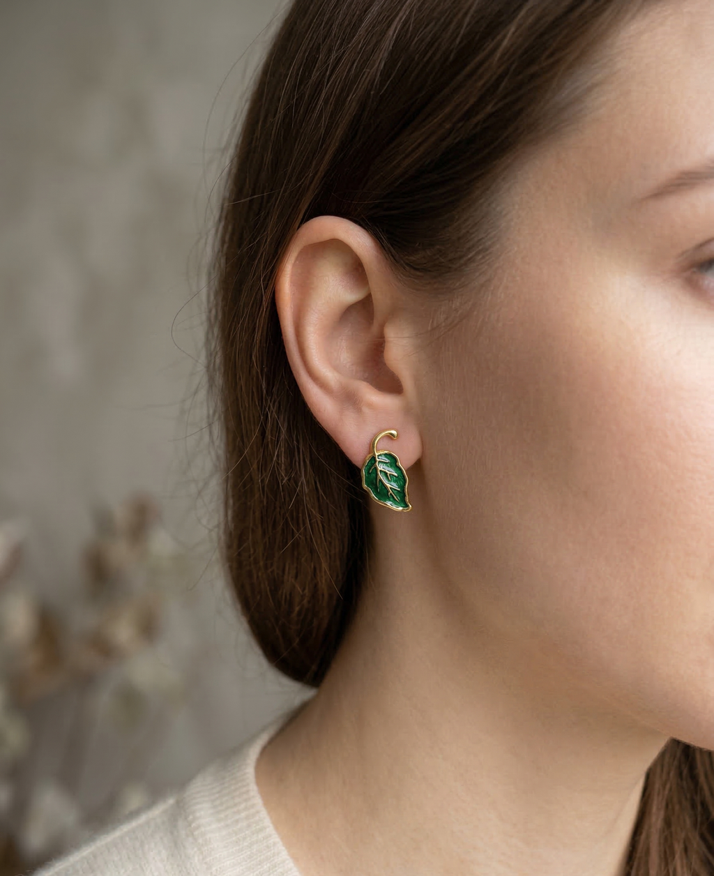 Close-up of a person wearing a green leaf-shaped earring with a neutral background
