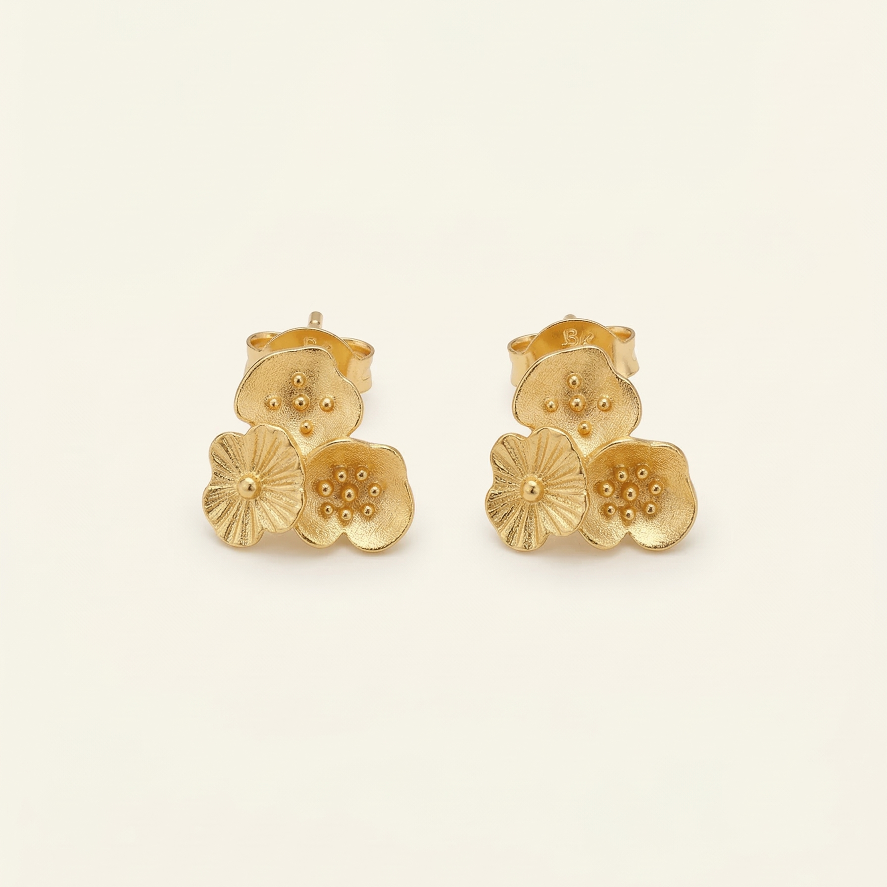Pair of gold floral earrings on a beige background