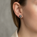 Close-up of an ear wearing a silver earring with black stones against a neutral background