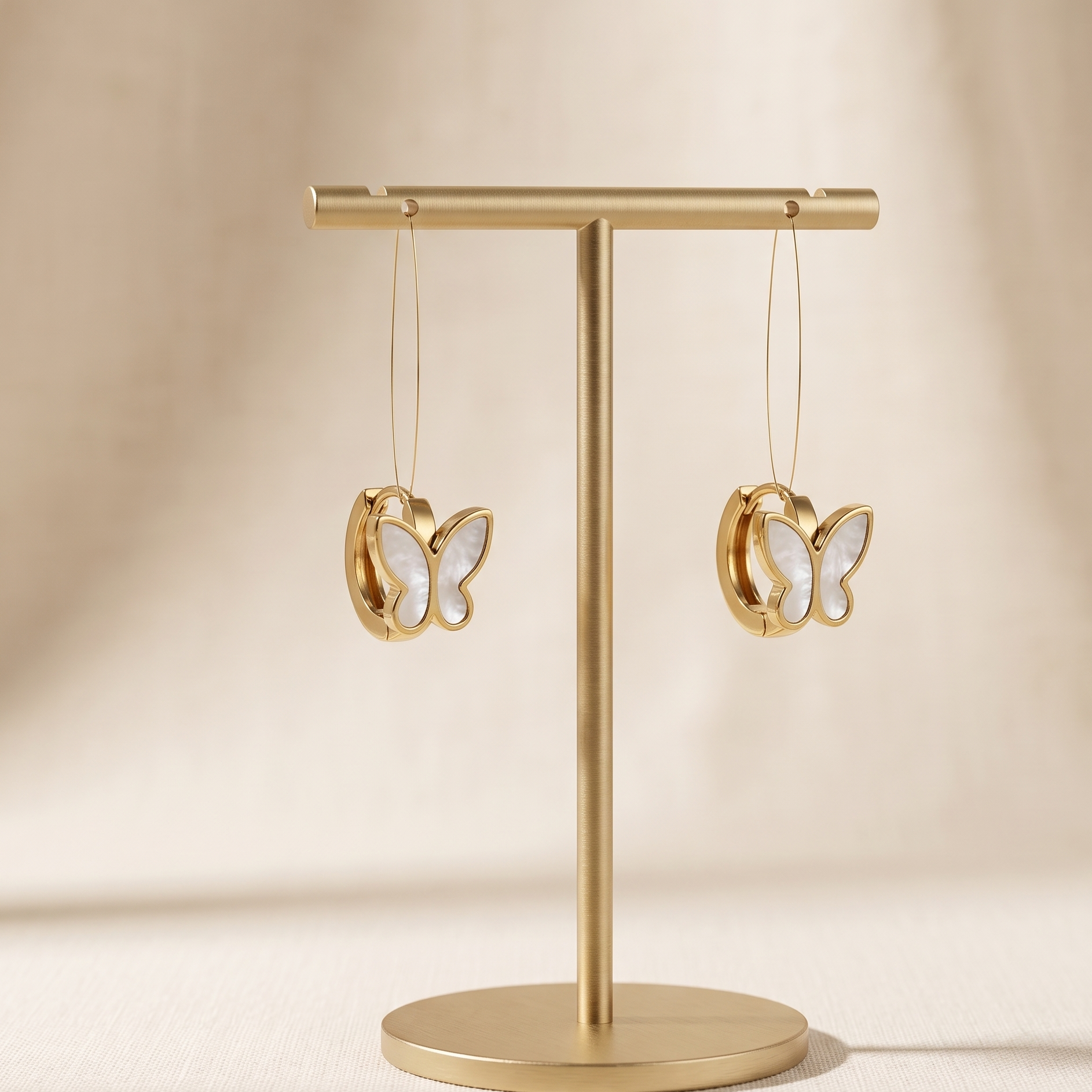 Gold earring stand with butterfly-shaped earrings on a beige background